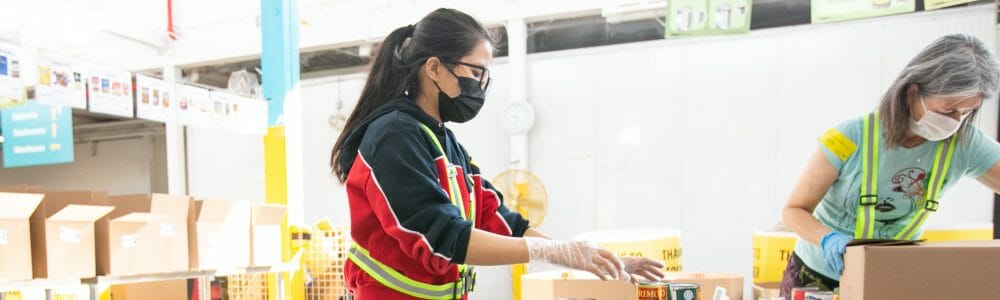 Image of two volunteers packing boxes with canned goods.