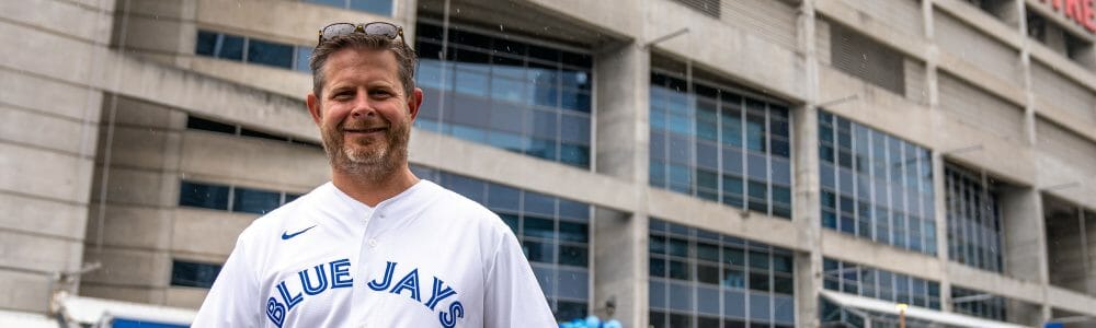 Image of Daily Bread CEO Neil Hetherington in Blue Jays jersey standing outside Rogers Centre