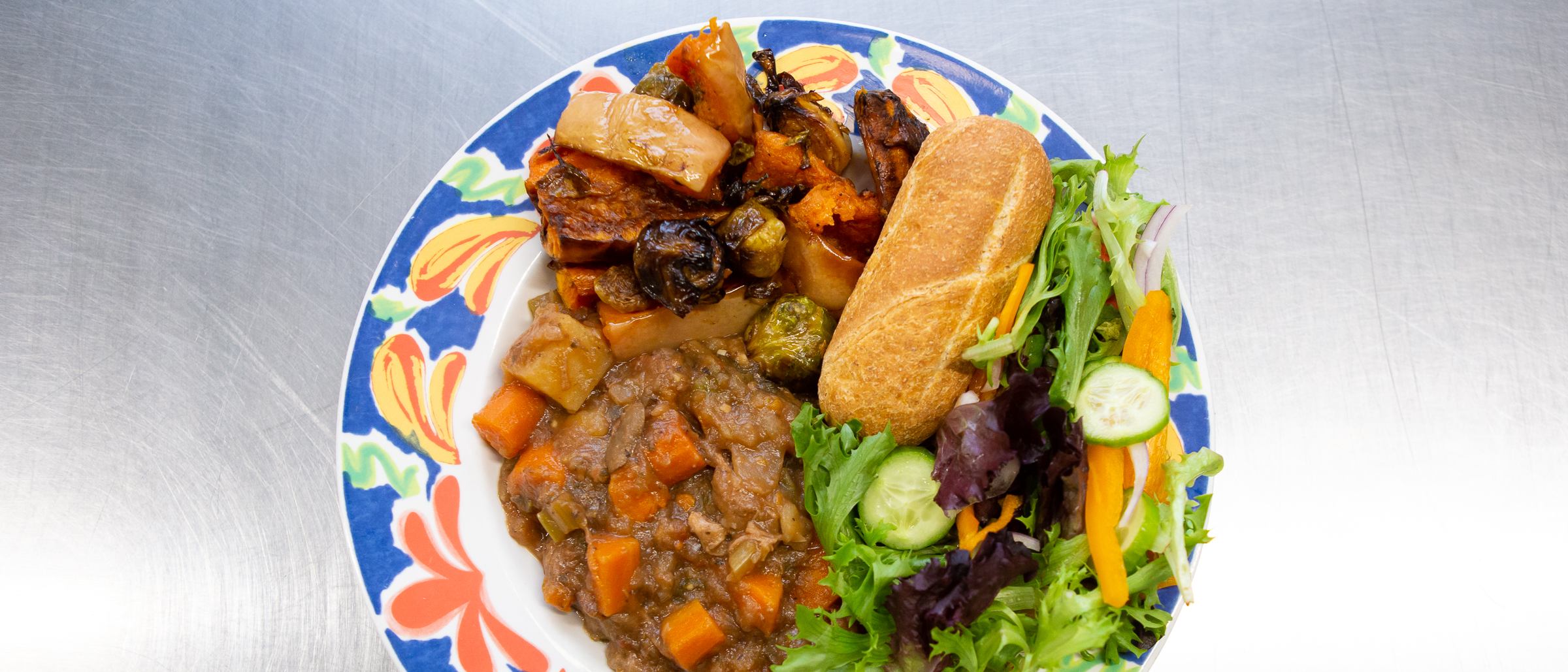 plate of stew, salad and bread roll on shiny table