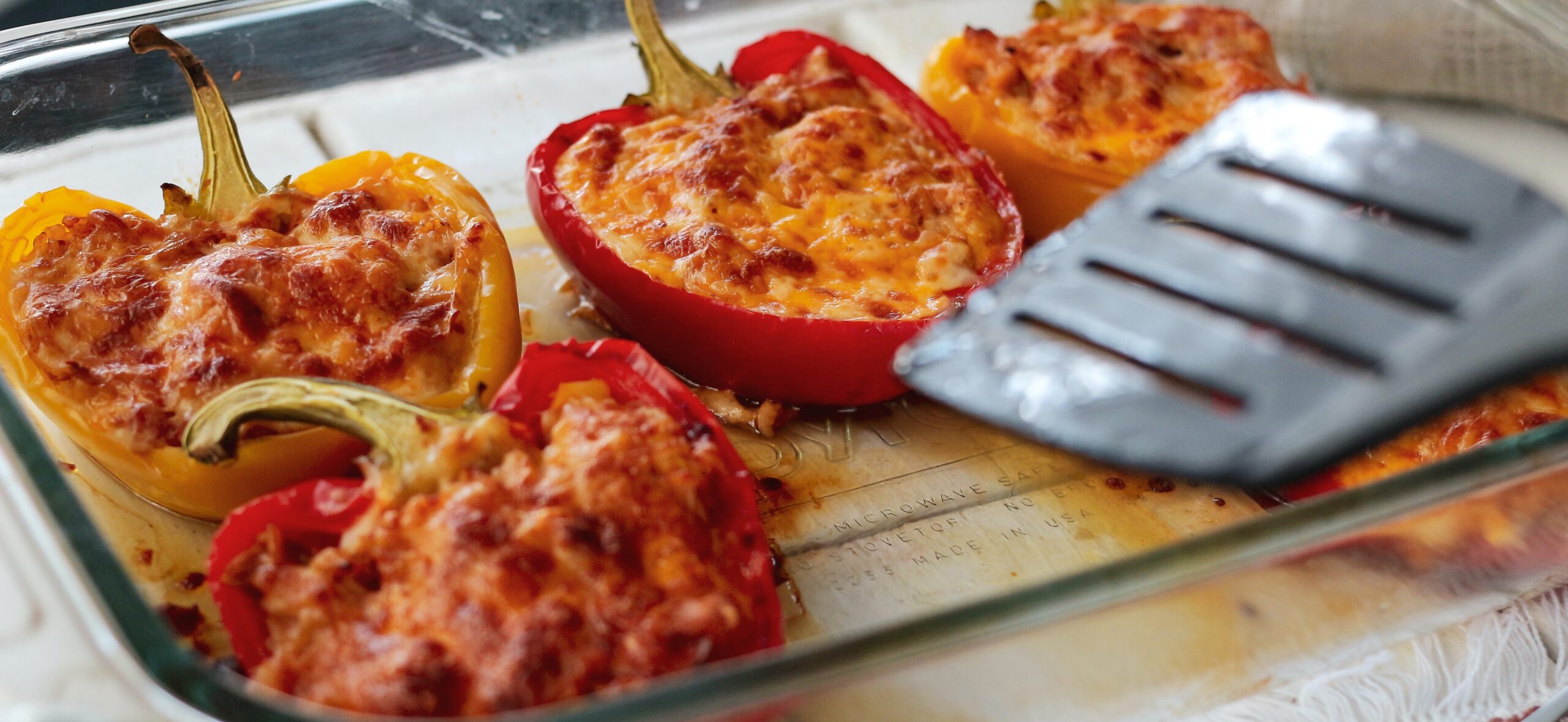 stuffed bell peppers with melted cheese in a glass baking dish with spatula